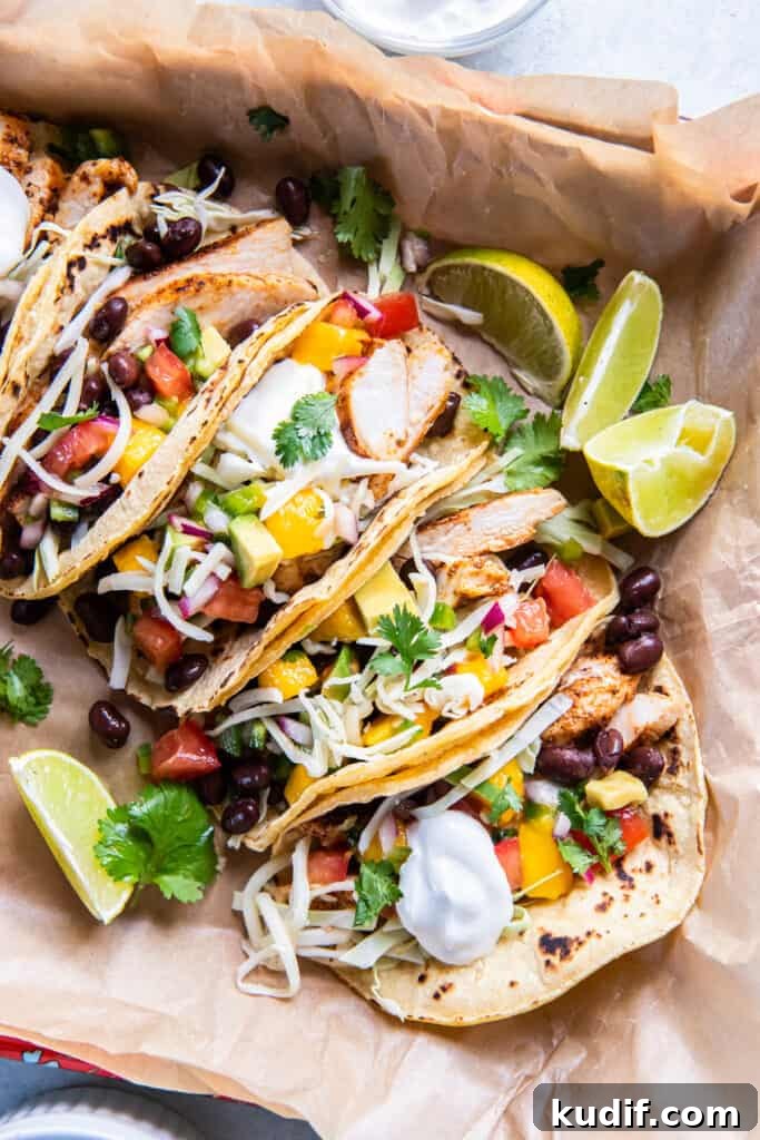A top down shot of chicken tacos with sour cream, cheese and mango salsa on parchment paper.
