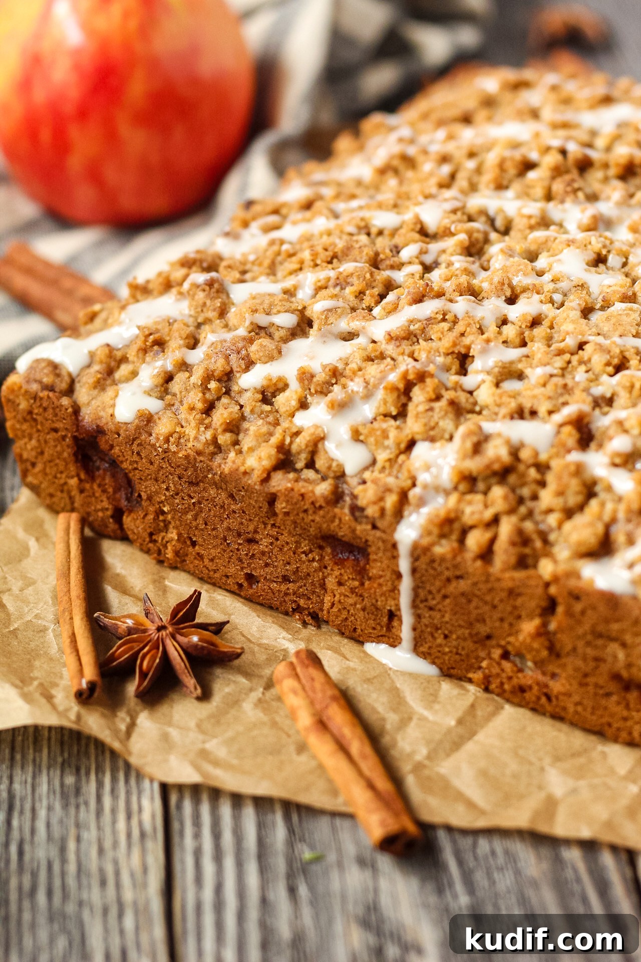 Spiced Apple Crumb Cake Recipe with Cinnamon Streusel 13 side shot of spiced apple crumb cake on wooden suface wiht an apple in the background.