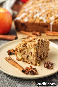 Spiced Apple Crumb Cake Recipe with Cinnamon Streusel 20 side shot of slice of apple crumb cake on a brown plate with apples and more cake in the background.