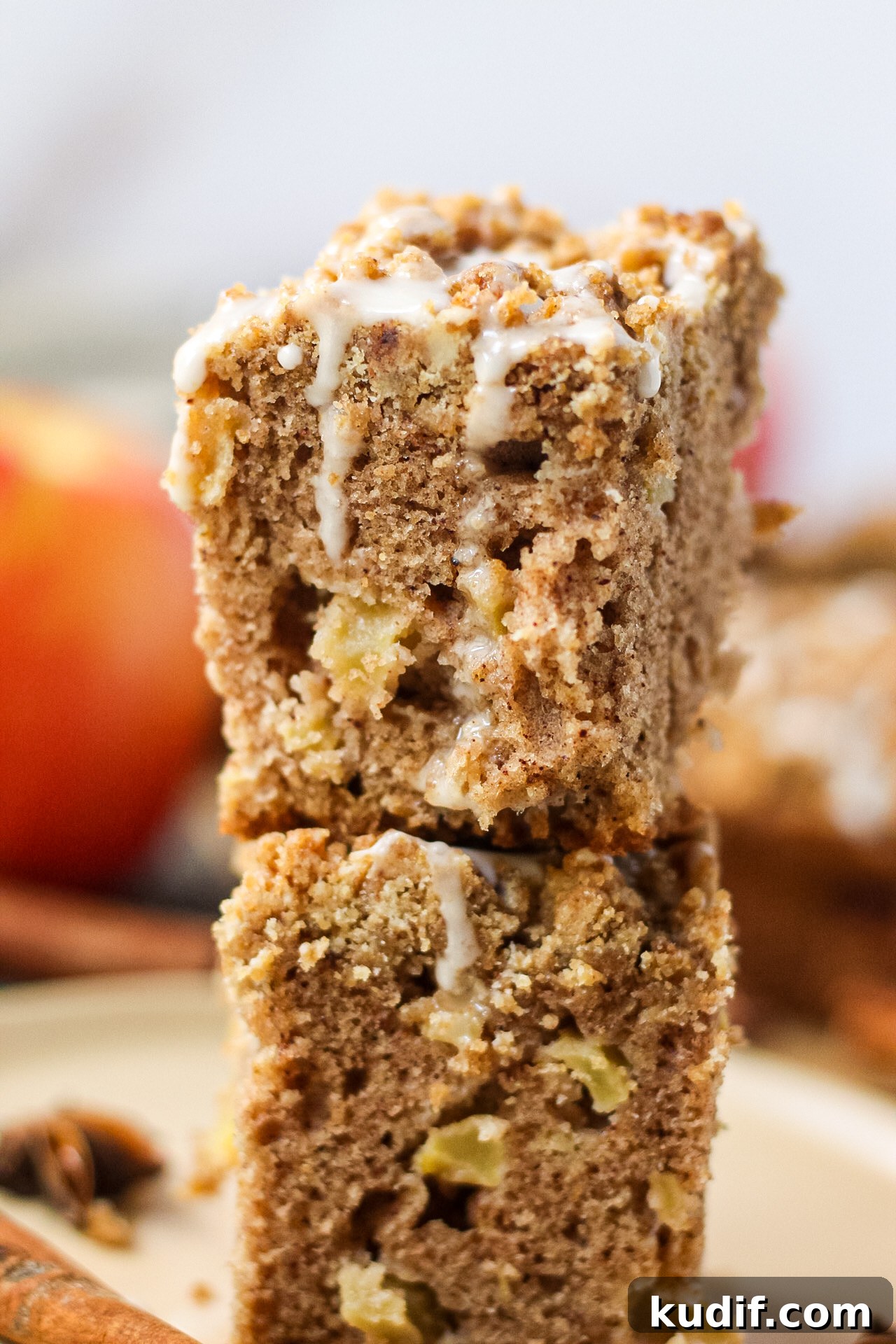 Spiced Apple Crumb Cake Recipe with Cinnamon Streusel 4 close up side shot of two slices of spiced apple crumb cake stacked on a brown plate with apples, cinnamon stick and star anise pods in the perimeter of shot.