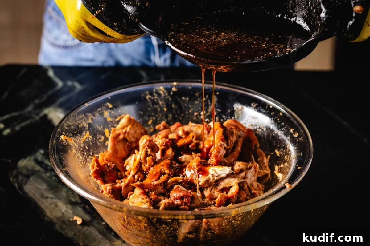 A chef's hands pouring juice from a cast iron skillet into a clear bowl of smoked poultry.