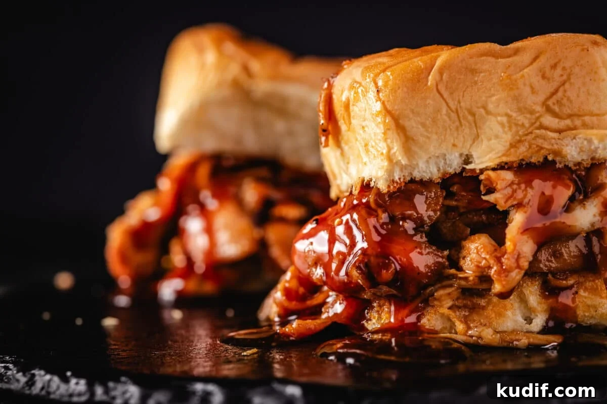 A closeup shot of 2 BBQ chicken sliders dripping with sauce.