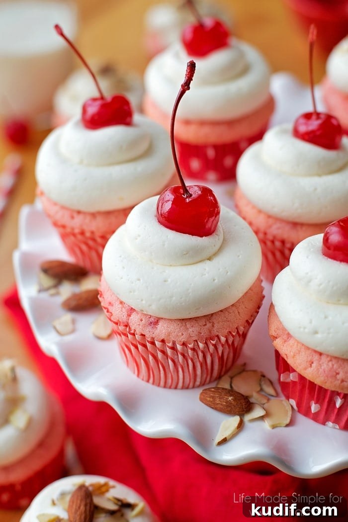 Cherry Almond Cupcakes with Cherry Glaze and Almond Crunch 6 Cherry almond cupcakes topped with maraschino cherries displayed on a white plate.