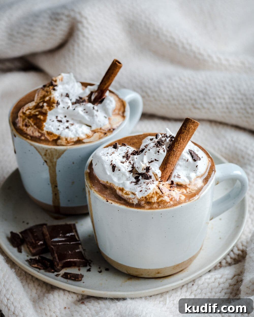 Vegan Gingerbread Hot Chocolate Recipe for Cozy Winter Nights 3 Side view of of hot chocolate in two white mugs on a white plate with chocolate squares on it.