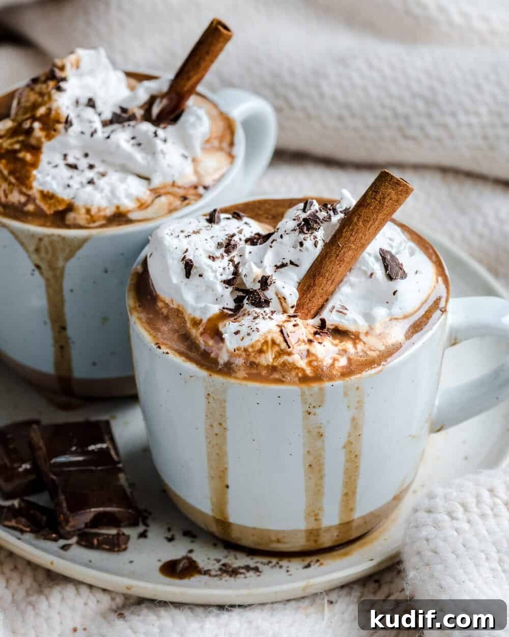 Vegan Gingerbread Hot Chocolate Recipe for Cozy Winter Nights 5 Side view of hot chocolate in two white mugs on a white plate with chocolate squares on it.