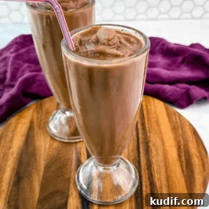 Two chocolate milkshakes served in classic soda fountain glasses on a wood platter, showing off the thick, frozen texture and striped straws.