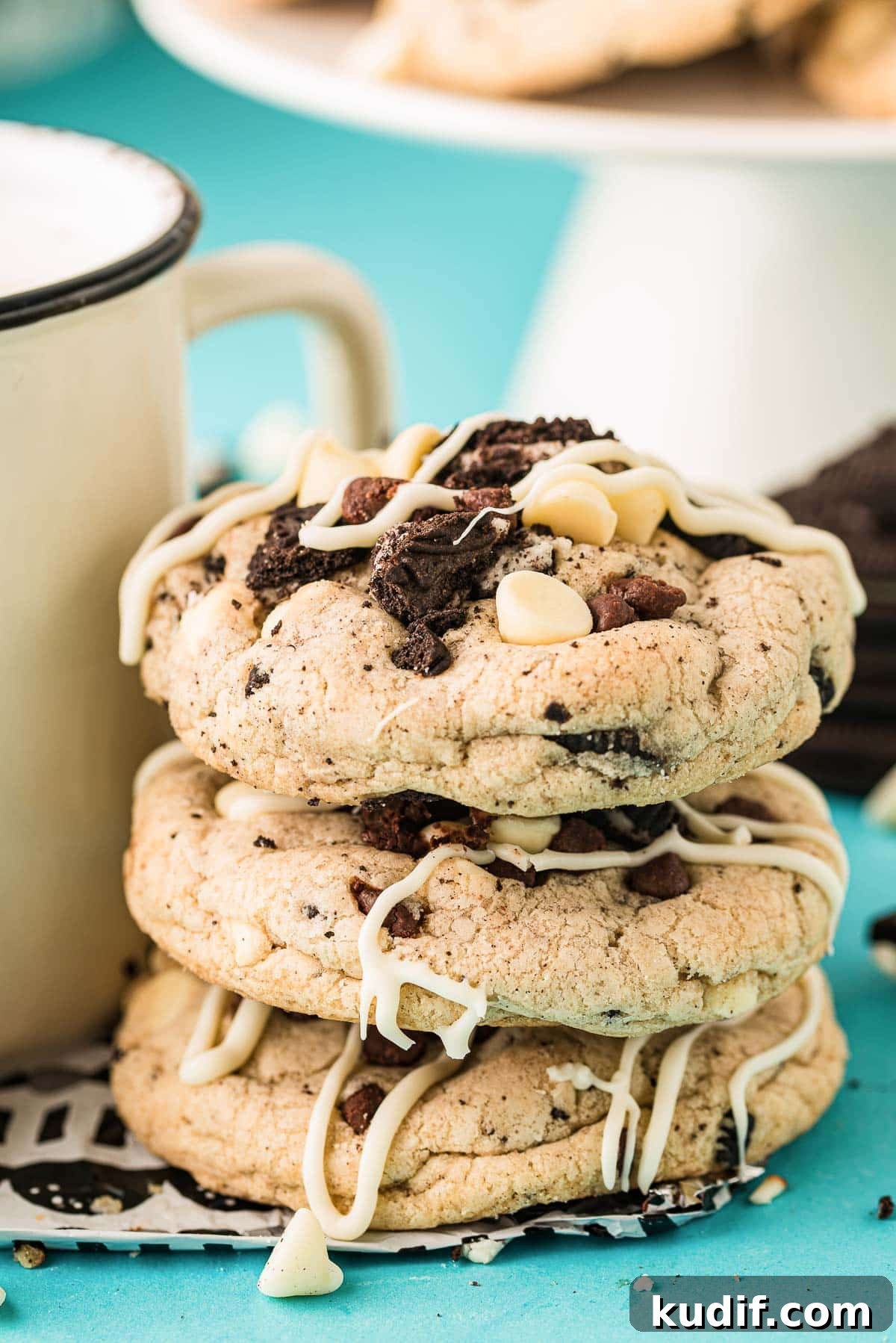 Chocolate chip oreo cookies stacked against a mug on a blue surface.