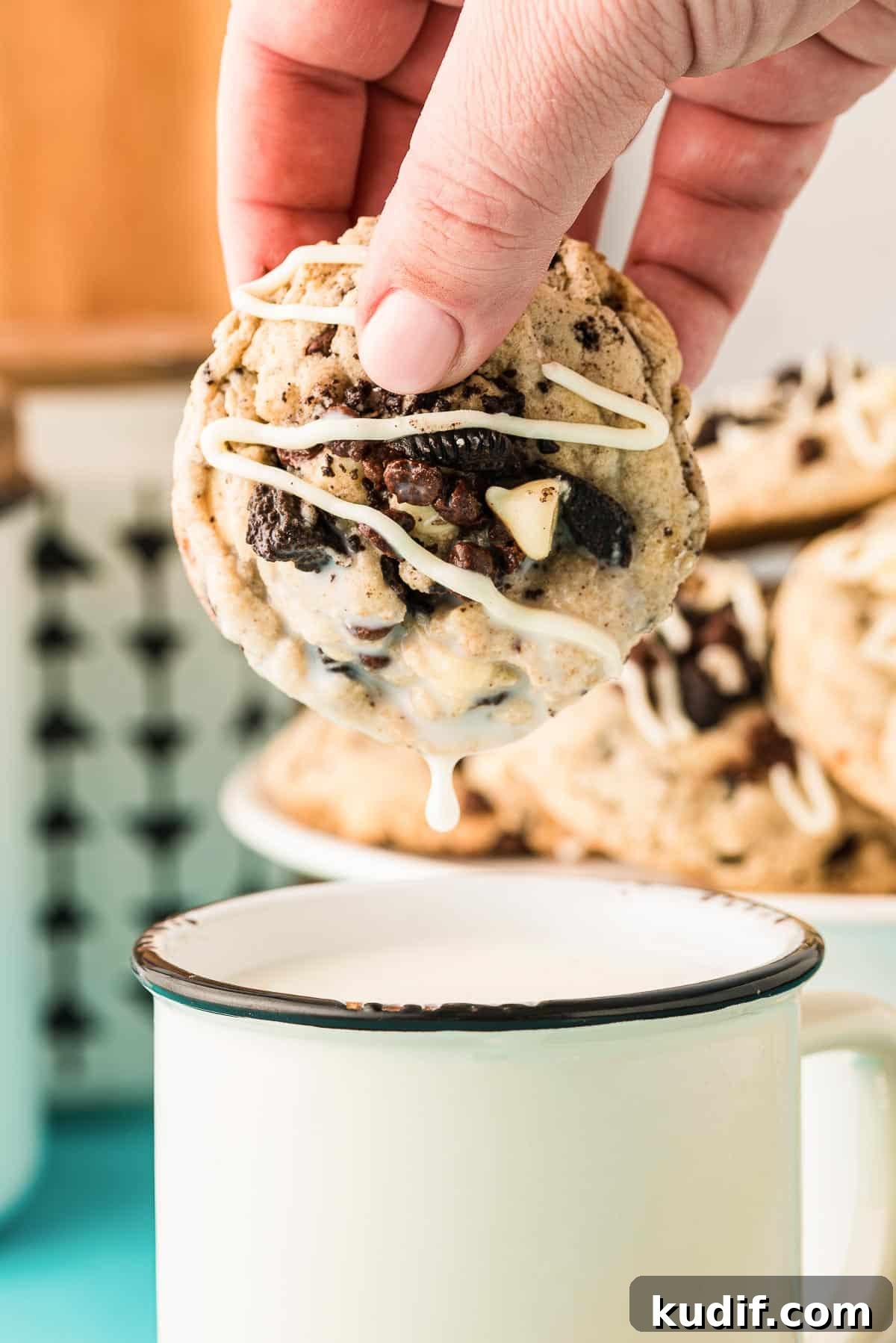 A woman's hand dipping an Oreo Chocolate Chip Cookie in a mug of milk.