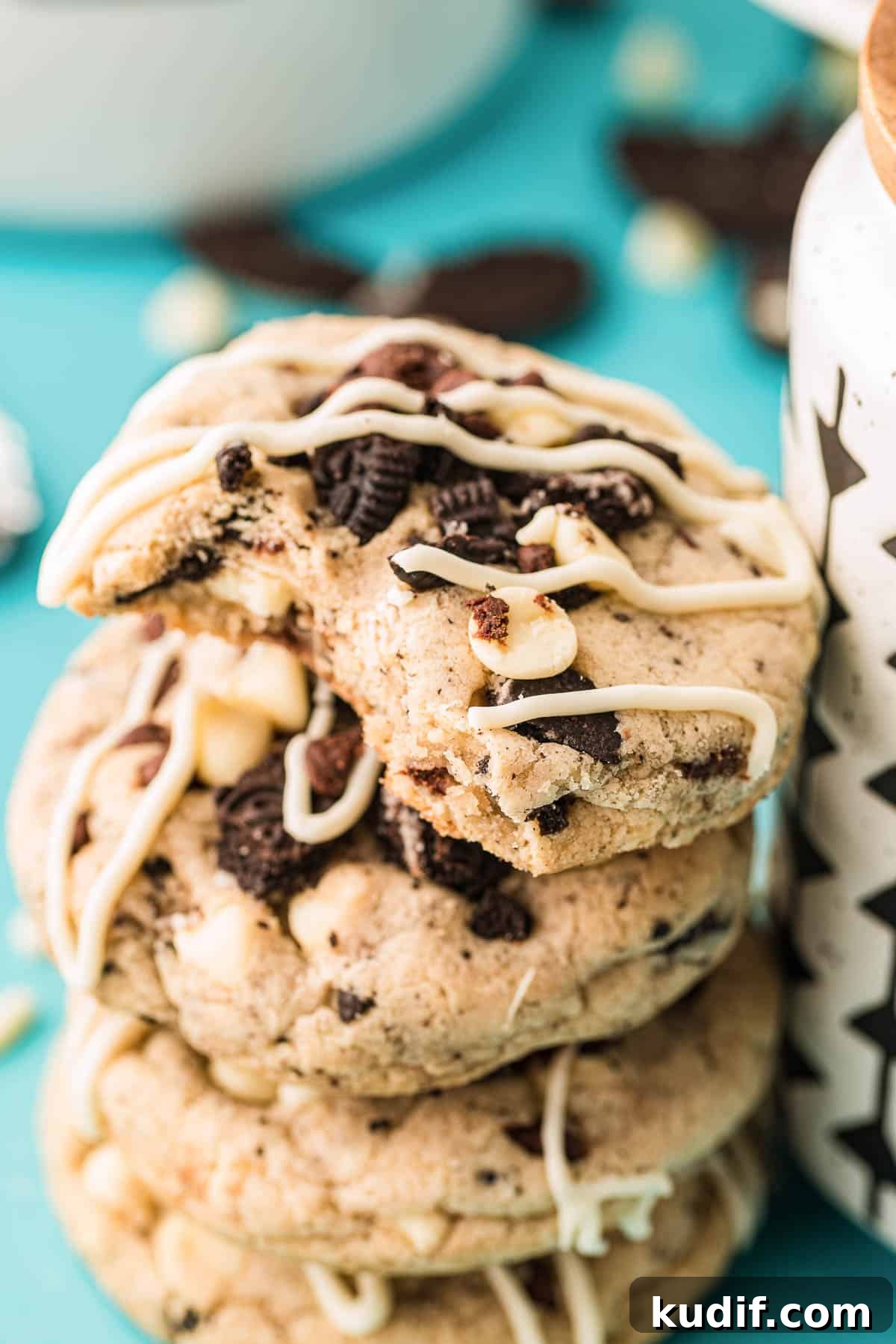 A stack of oreo chocolate chip cookies leaning against a mug with the top one missing a bite.