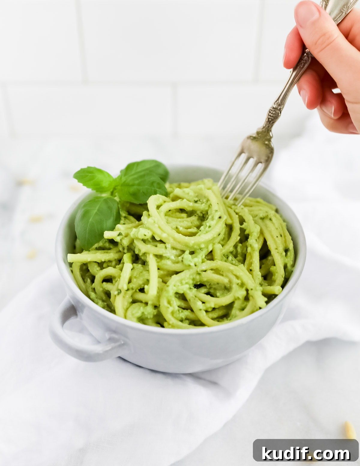 Creamy Pesto Sauce Recipe: Rich Basil Sauce for Pasta & More 5 A hand with a fork reaching into a bowl of green pesto over spaghetti