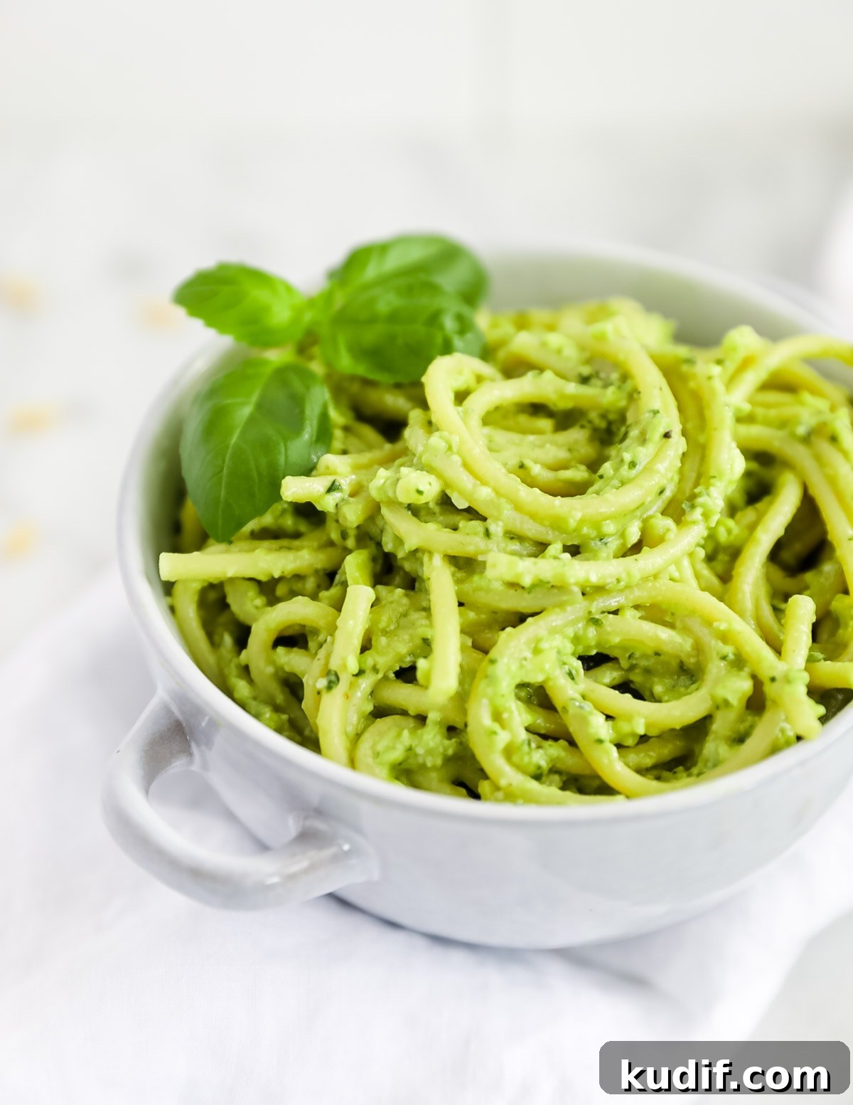 Creamy Pesto Sauce Recipe: Rich Basil Sauce for Pasta & More 6 Creamy green pesto over spaghetti noodles, served in a blue bowl and garnished with fresh basil leaves