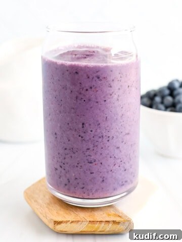 A blueberry smoothie in a clear cup.