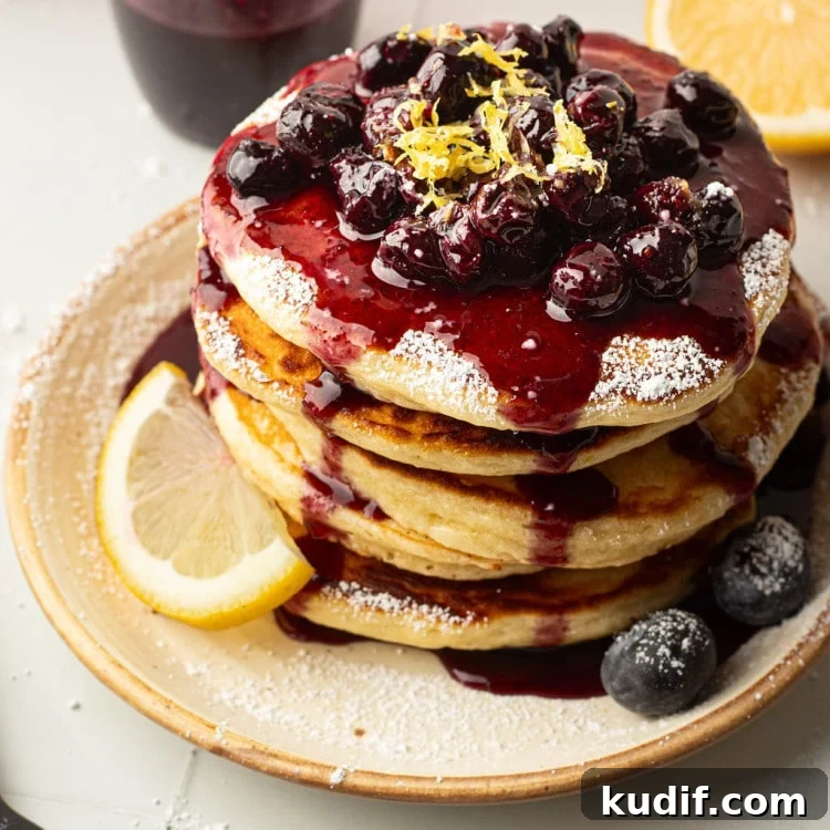 A top-down view of a pancake stack covered in blueberry compote, powdered sugar, and lemon zest.