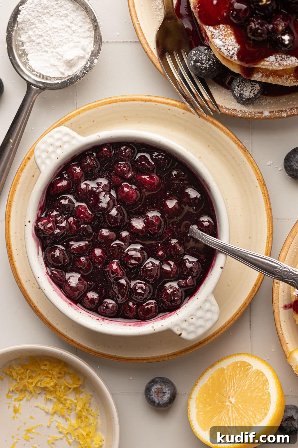Lemon Pancakes with Blueberry Maple Syrup Recipe 6 A close-up of a bowl filled with glossy blueberry compote, with a spoon resting inside.