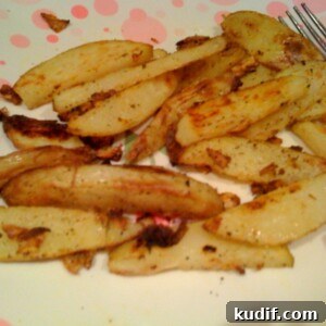 Cajun Garlic Oven-Baked Fries That Crisp Every Time 3 Close up of baked garlic cajun fries on a white plate, a fork in the background