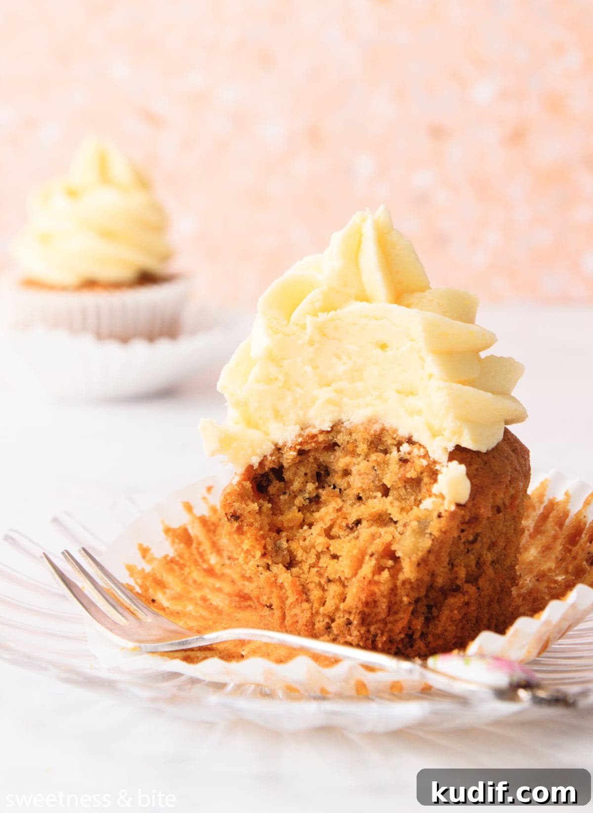 A carrot cupcake with a bite taken out of it, sitting on the peeled cupcake liner.