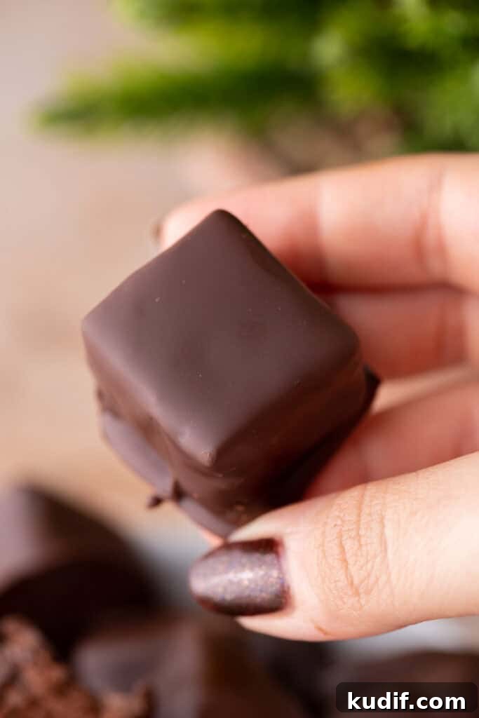 A hand holding a freshly dipped chocolate candy square with a smooth coating.