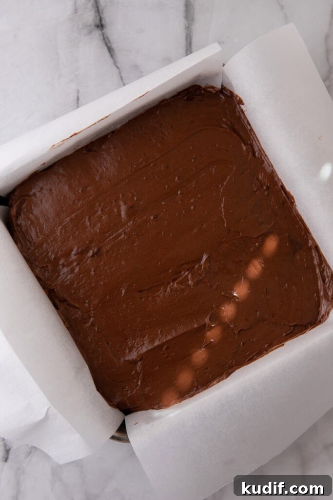 Chocolate candy filling spread evenly in a parchment-lined square baking dish before freezing.