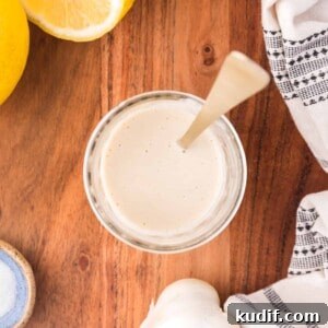 Overhead view of tahini sauce in a small jar, with a spoon.