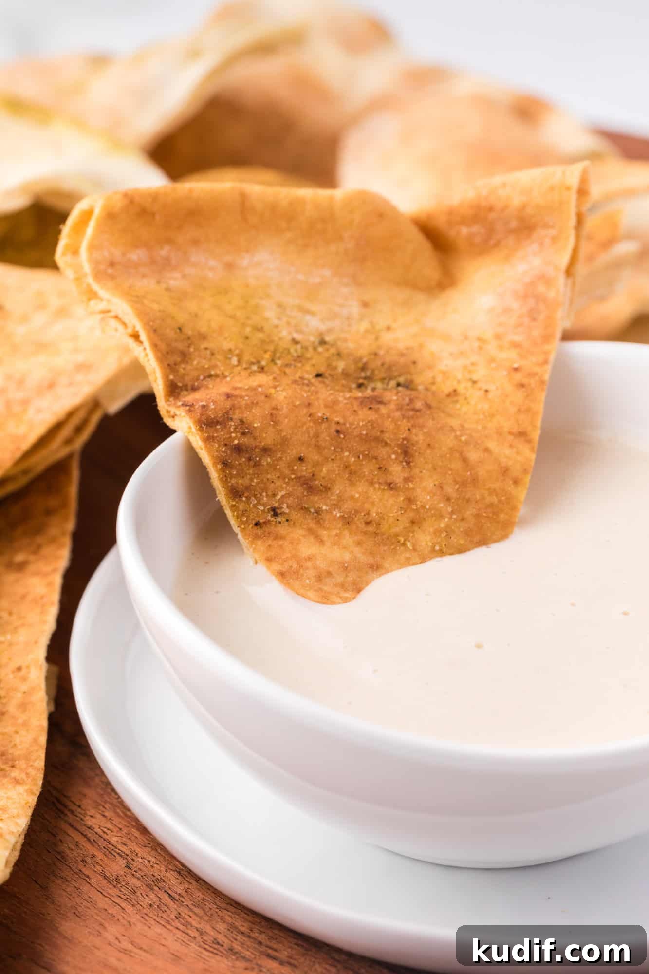 A pita chip resting in a bowl of tahini sauce.