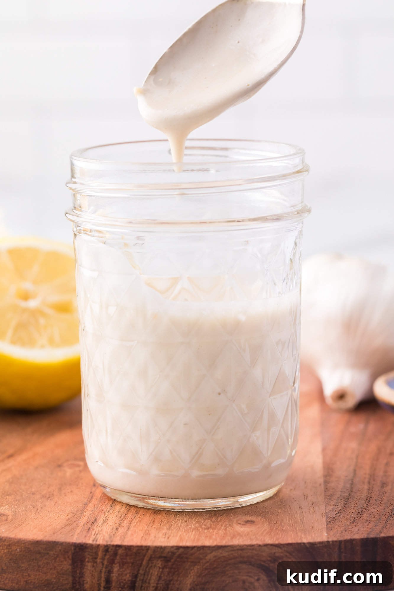 A spoon drizzling tahini sauce into a mason jar.