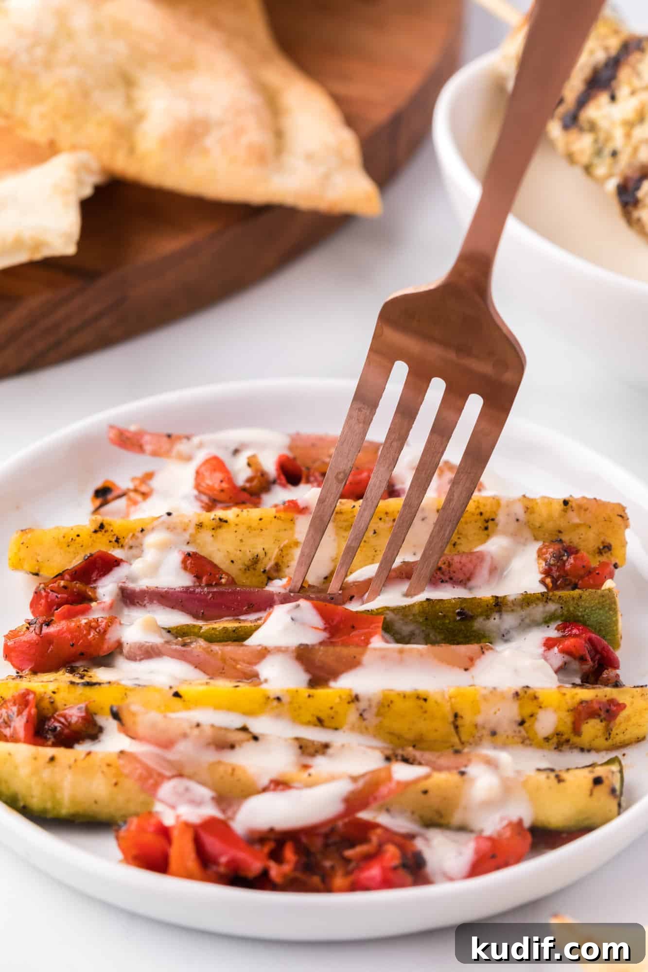 A fork picking up veggies drizzled with tahini sauce from a plate.