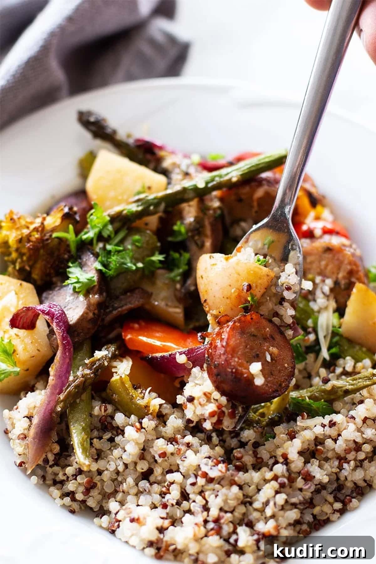 Sheet Pan Sausage with Roasted Vegetables Recipe 11 Fork containing smoked sausage with fresh baked potatoes, asparagus, and broccoli, served with cooked quinoa.