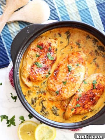 Black pan containing 3 Lemon Butter Chicken Breasts, crossed spoons and lemon slices on table.