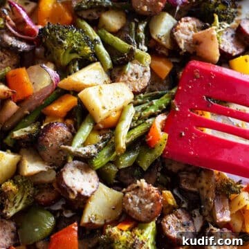 Person serving sausage and vegetables from a sheet pan for dinner.