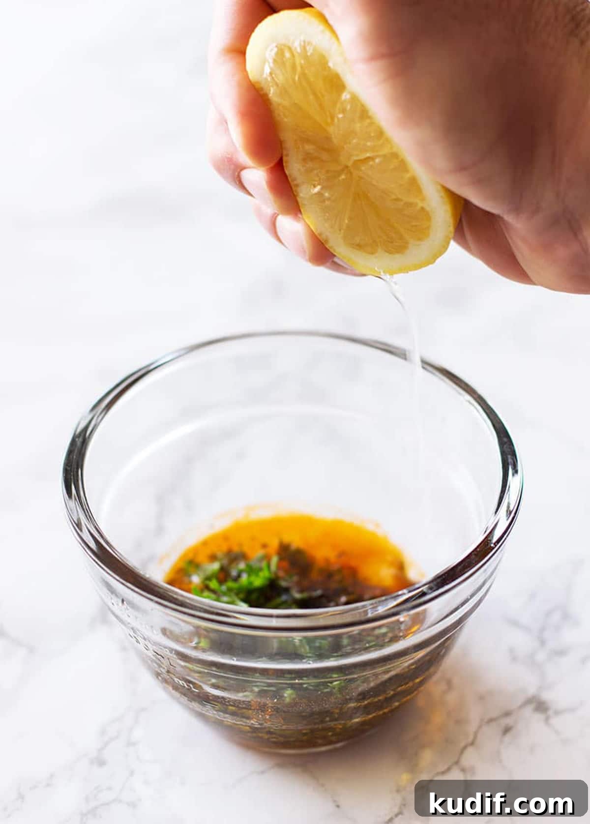 Sheet Pan Sausage with Roasted Vegetables Recipe 7 Hand squeezing a lemon into a glass bowl for a lemon herb marinade.