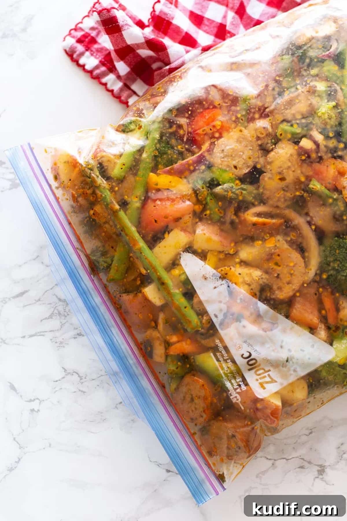 Sheet Pan Sausage with Roasted Vegetables Recipe 8 Ziplock bag containing One Pan Smoked Sausage and Vegetables in a lemon herb marinade sitting on white marble counter.