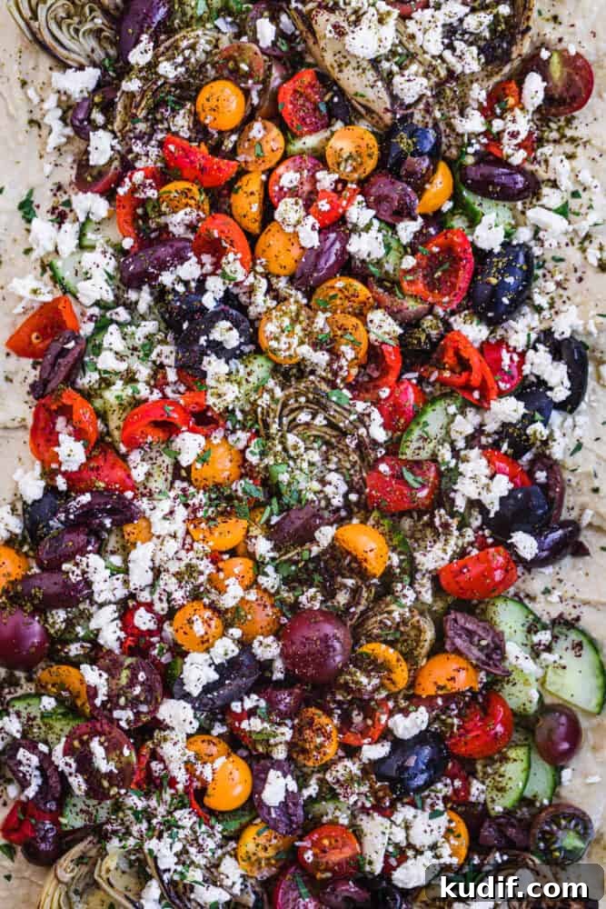 Loaded Hummus: Mediterranean 7-Layer Dip with Veggies & Feta 3 loaded hummus with veggies, cheese, herbs, spice and more; overhead.