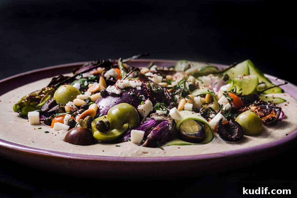 Loaded Hummus: Mediterranean 7-Layer Dip with Veggies & Feta 8 hummus loaded with toppings on a pink plate and dark background; side angle.