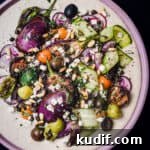 Loaded Hummus: Mediterranean 7-Layer Dip with Veggies & Feta 10 Loaded hummus topped with cucumbers, tomatoes, olives, eggplant, capers, radishes, feta, pine nuts, and fresh herbs. Overhead shot.