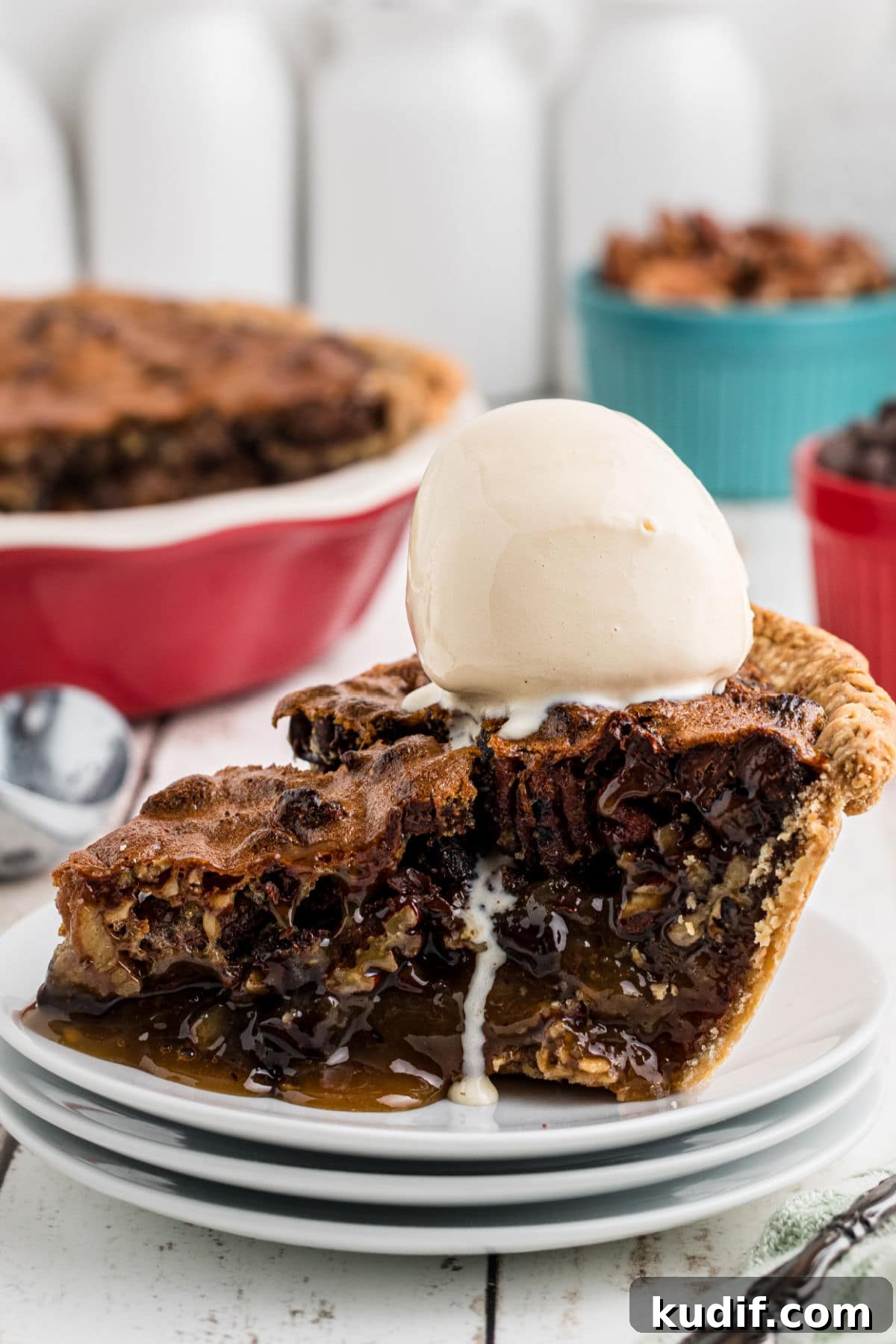 Decadent Chocolate Bourbon Pecan Pie Recipe 9 A slice of chocolate bourbon pecan pie on a plate with a shiny scoop of ice cream on top. The angle of the photo highlights the gooey, chocolate interior of the pie which runs a little onto the plate.