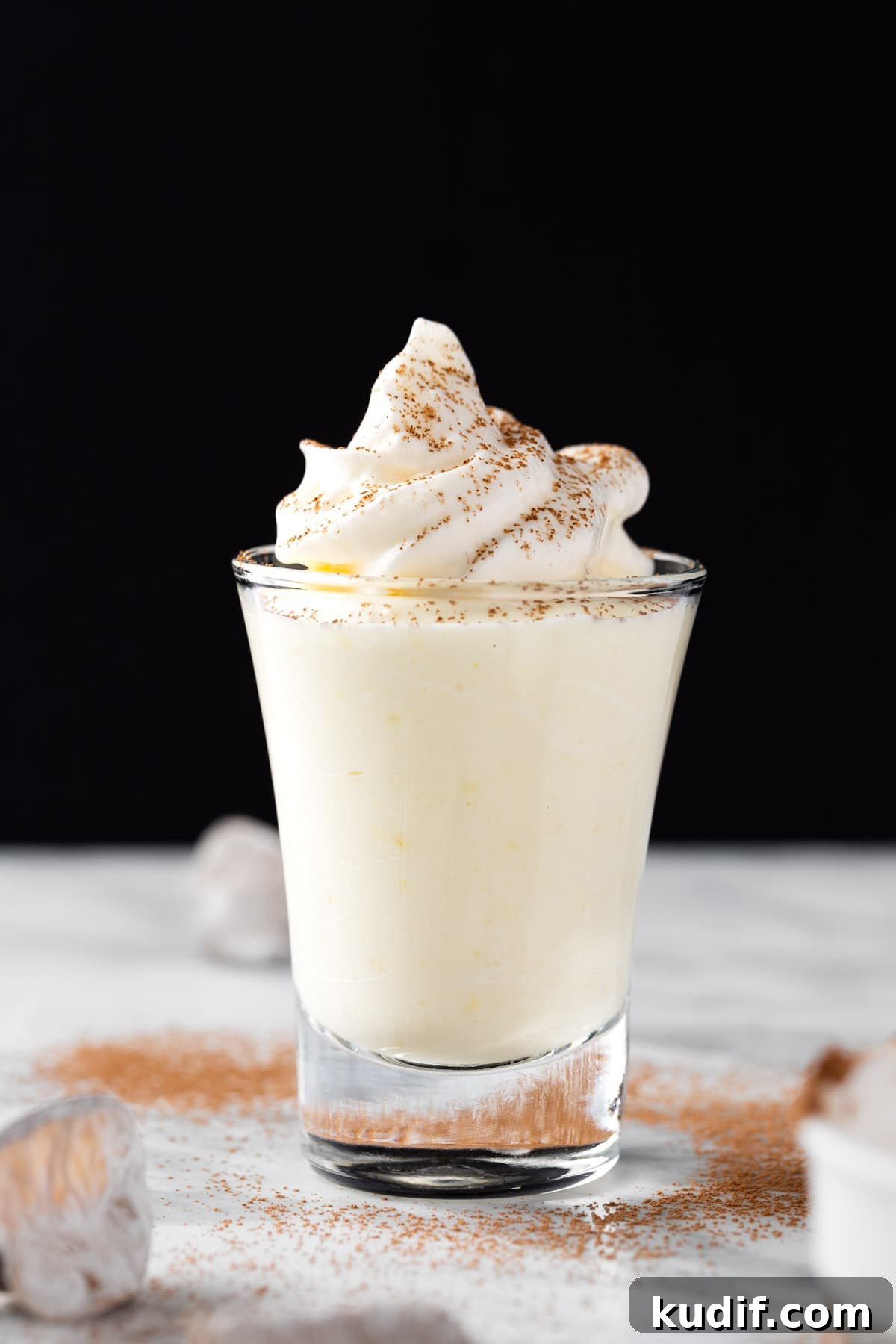 Creamy Vanilla Pudding Shots Recipe for Parties 2 Vanilla pudding shots topped with whipped cream, on a black background.